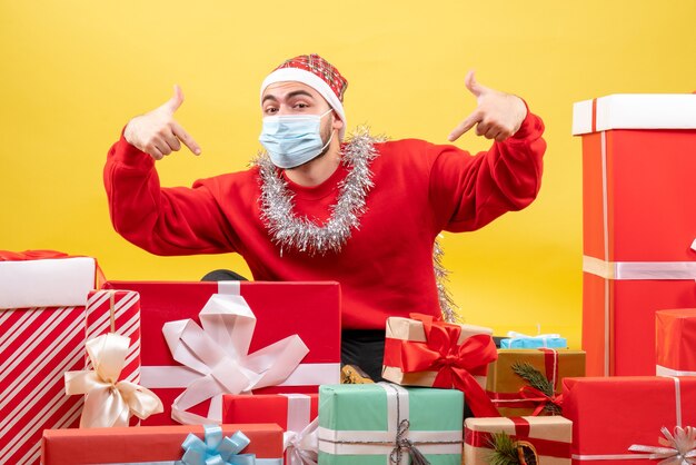 Front view young male sitting around presents on yellow background