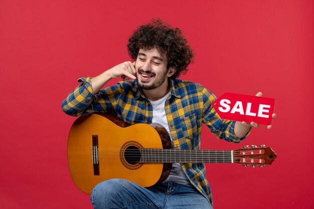 Free Photo front view young male sitting with guitar on red wall color applause live musician concert sale play