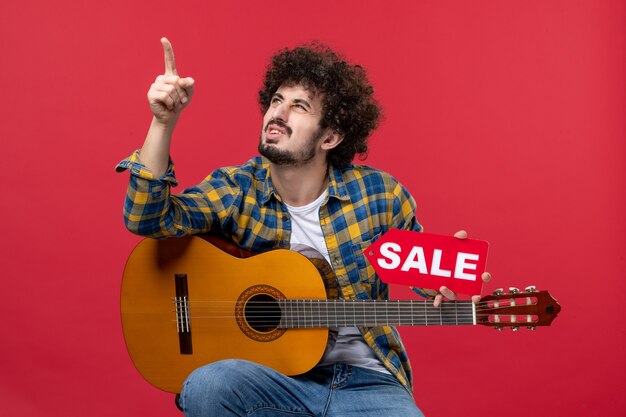 Front view young male sitting with guitar on red wall concert live music color applause musician play