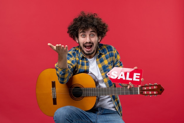 Free Photo front view young male sitting with guitar on a red wall concert live musician sale play music color applause