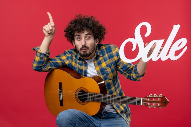 Free Photo front view young male sitting with guitar on the red wall music concert applause live musician color sale