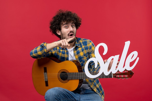 Free Photo front view young male sitting with guitar on red wall play concert musician sale color applause live