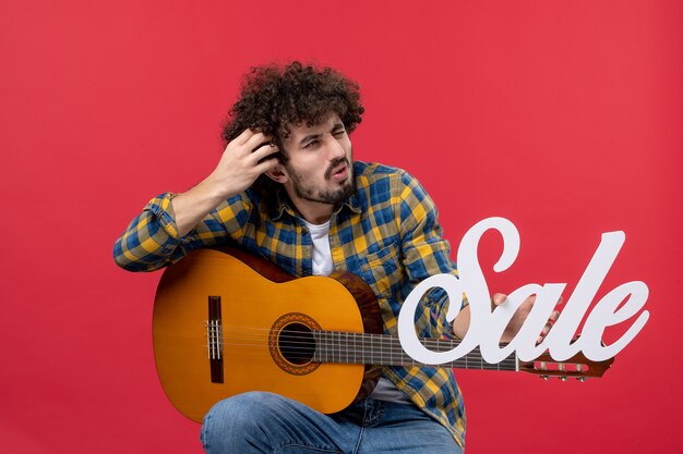 Front view young male sitting with guitar on the red wall sale play concert music color applause live musician