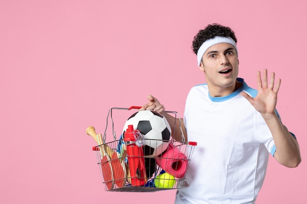 Free photo front view young male in sport clothes with basket full of sport things pink wall