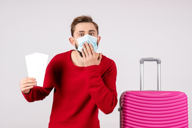 Front view young male in sterile mask holding tickets on white wall voyage covid- flight trip vacation virus color emotion