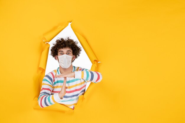 Front view young male in sterile mask showing t sign on yellow health color photo covid- pandemic virus human