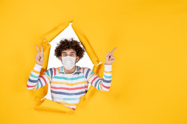 Front view young male in sterile mask on a yellow ripped color covid- health human pandemic virus photo