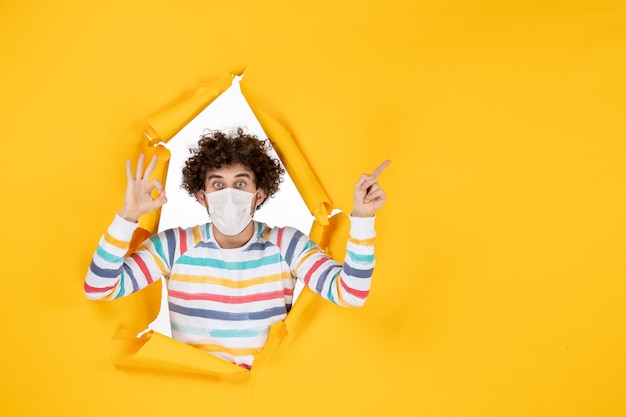 Front view young male in sterile mask on yellow ripped color covid- health human pandemic virus photo