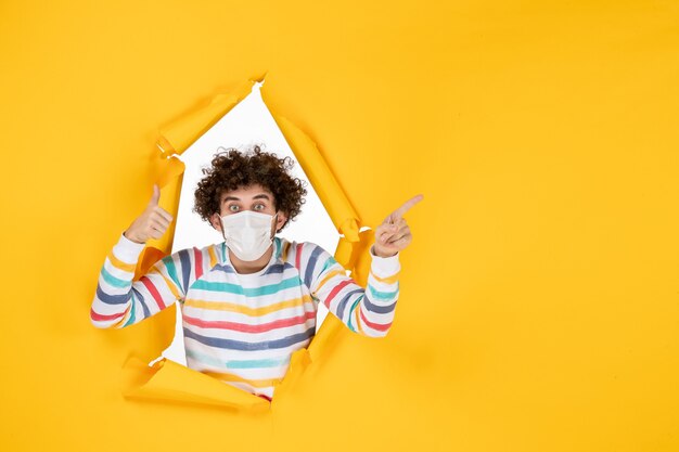 Front view young male in sterile mask on a yellow ripped color covid- health human photo pandemic virus