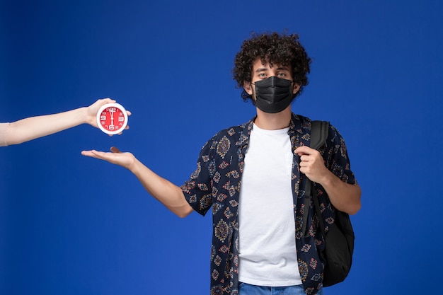 Free photo front view young male student wearing black mask with backpack on light blue background.