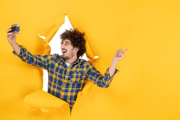 Front view young male taking photo with camera on yellow background