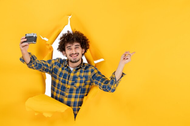 Front view young male taking photo with camera on yellow background