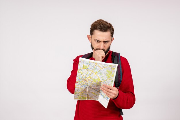 Front view young male tourist with backpack exploring map on white wall plane city vacation emotion color tourism route