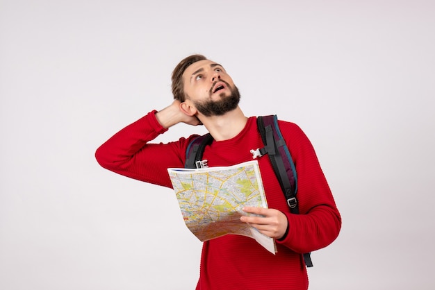 Front view young male tourist with backpack exploring map on the white wall plane city vacation emotion human color tourism