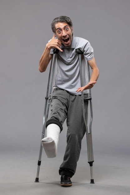 Front view young male using crutches due to broken foot on grey floor pain foot disable accident leg broken