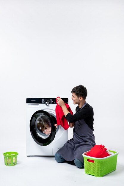 Front view of young male washing clothes with the help of washing machine on white wall