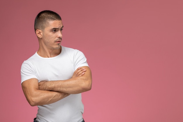 Front view young male in white shirt posing with crossed hands on pink background