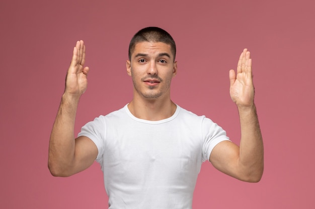 Front view young male in white shirt posing with his hands on the pink background