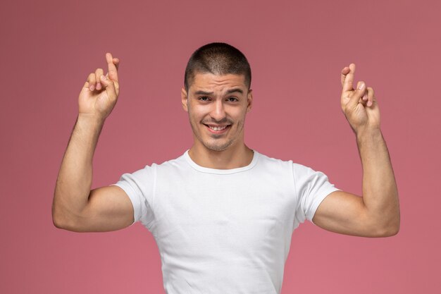 Front view young male in white shirt smiling with crossed fingers on pink background 