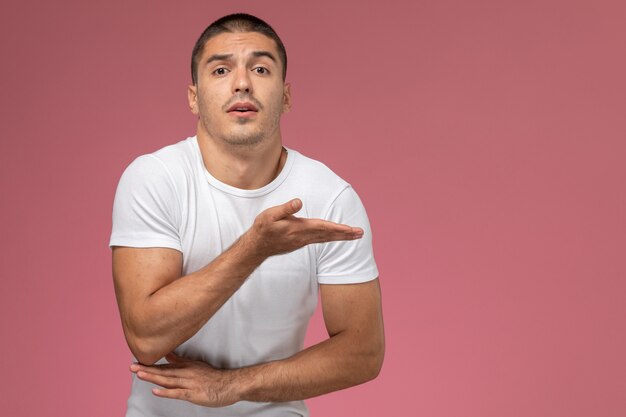 Front view young male in white shirt with raised hand on the pink background 