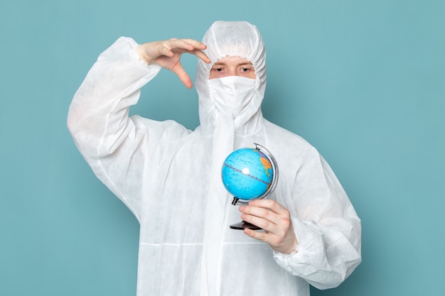 Free photo a front view young male in white special suit and holding little globe on the blue wall man suit danger special equipment color