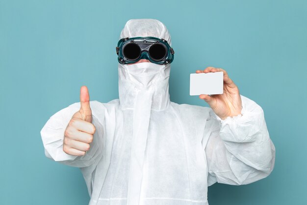 A front view young male in white special suit and holding white card on the blue wall man suit danger special equipment color