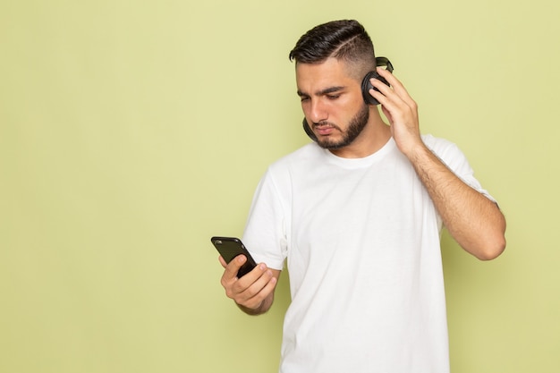 A front view young male in white t-shirt holding phone and listening to music