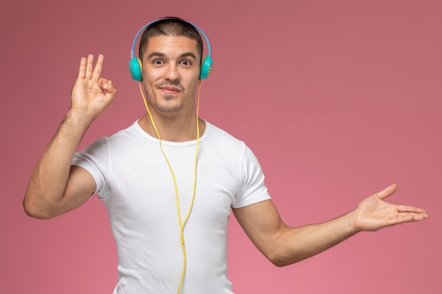 Free photo front view young male in white t-shirt listening to music via his earphones on the light-pink background