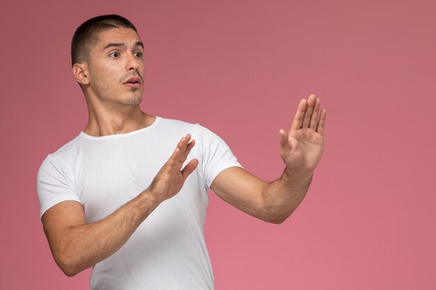 Front view young male in white t-shirt posing with cautious expression on pink background 