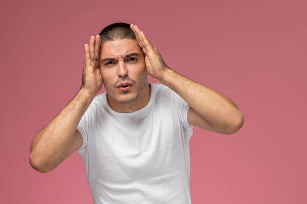 Front view young male in white t-shirt posing with confused expression on pink desk 