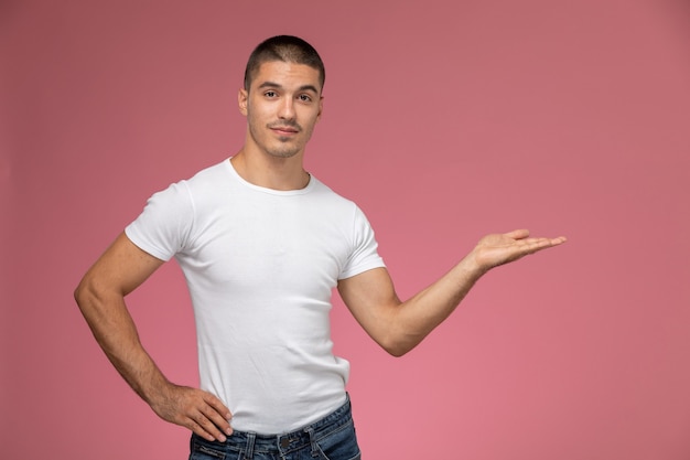 Front view young male in white t-shirt posing with raised palm on pink background 