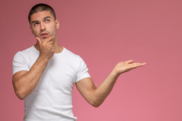 Front view young male in white t-shirt posing with thinking expression on pink background  