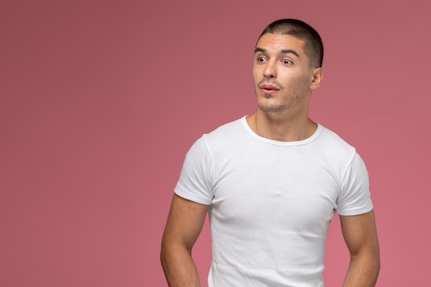 Front view young male in white t-shirt simply posing on the pink background 