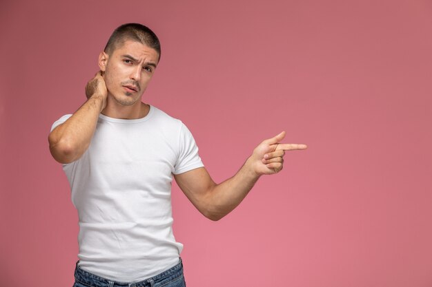 Front view young male in white t-shirt suffering from neck ache on pink desk  