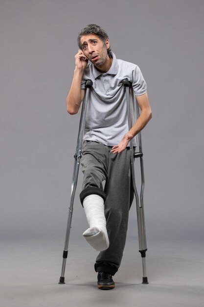 Front view young male with crutches due to broken foot on grey desk disable foot broken accident leg