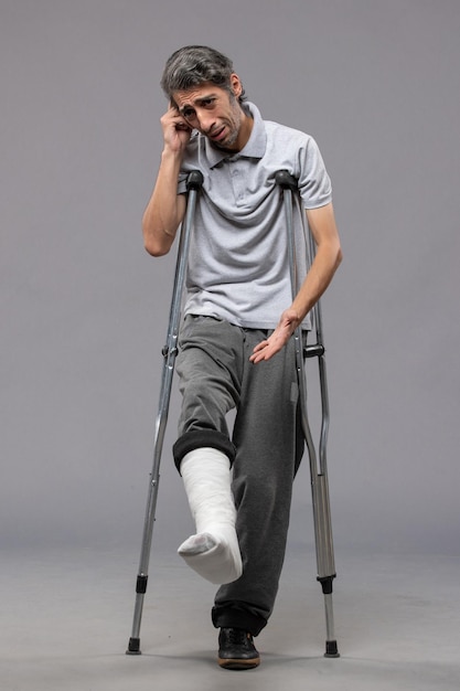 Front view young male with crutches due to broken foot on the grey wall disable foot broken accident leg