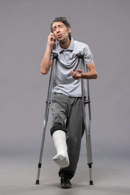 Front view young male with crutches due to broken foot on grey wall disable foot broken accident legs