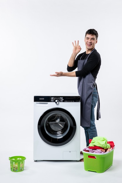 Front view of young male with dirty clothes and washer on white wall