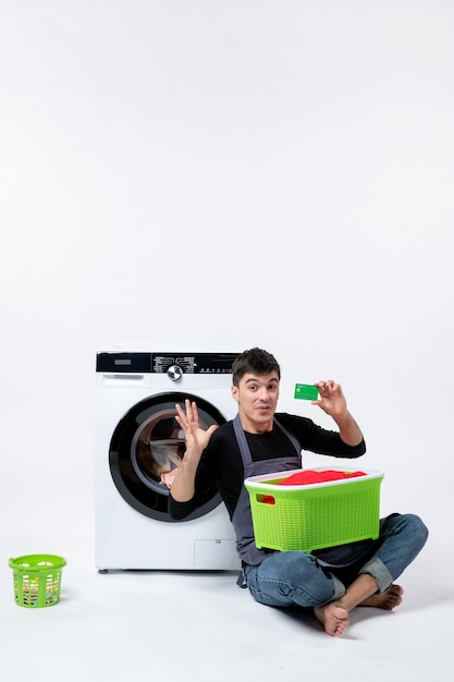 Free photo front view of young male with green basket full of clothes holding bank card on white wall