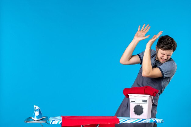 Front view young male with ironing board on blue background laundry iron color washing machine cleaning man