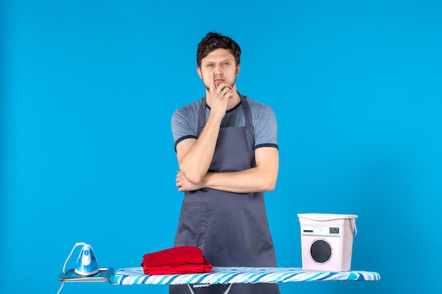 Free photo front view young male with ironing board thinking on blue background housework laundry cleaning washing machine man color iron