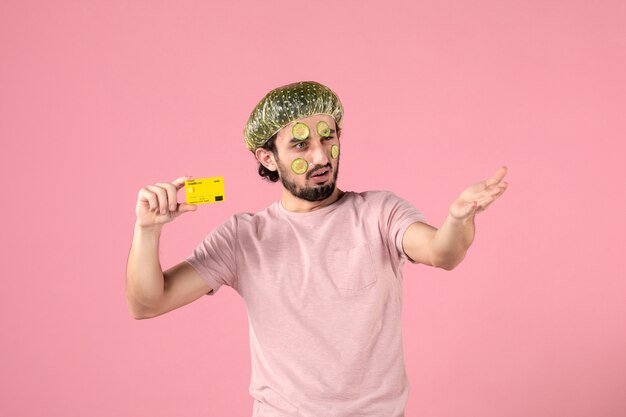 Free photo front view young male with mask on his face holding bank card on pink background