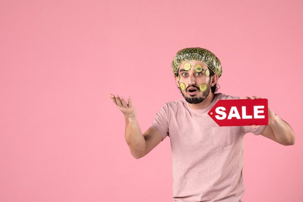 Free Photo front view young male with mask on his face holding sale nameplate on pink background