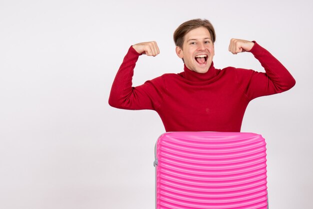 Front view of young male with pink bag flexing on white wall