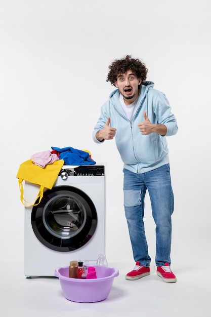 Front view of young male with washer and dirty clothes on a white wall