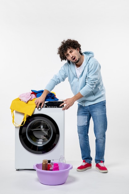 Front view of young male with washer and dirty clothes on white wall