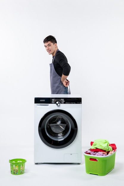 Front view of young male with washer and dirty clothes on white wall