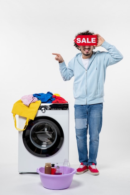 Front view of young male with washer holding red sale banner on white wall