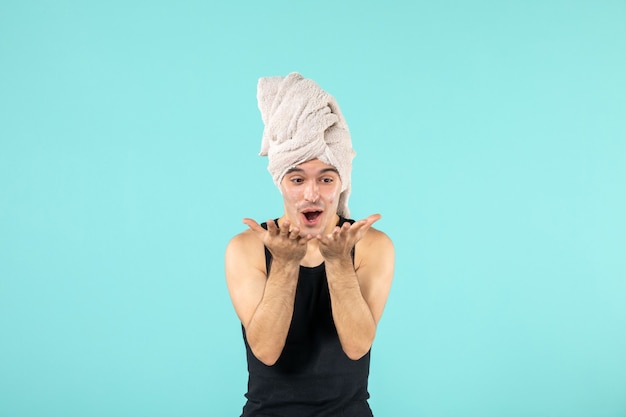 front view of young man after shower applying cream to his face on blue wall