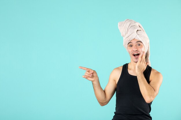 front view of young man after shower applying cream to his face on blue wall